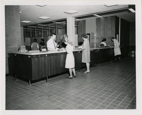 Library employees assisting patrons at circulation desk, ca. 1964