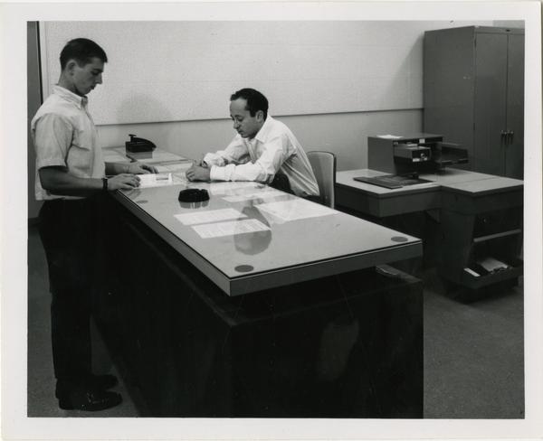 Librarian assisting patron at desk, ca. 1964