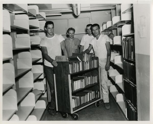Group of workers pose during the process of loading books on truck for University Research Library move, 1964