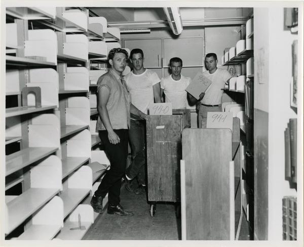 Group of workers pose during the process of loading books on truck for University Research Library move, 1964