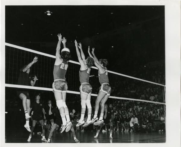 Three UCLA volleyball players attempting to block the ball in front of the net during a game