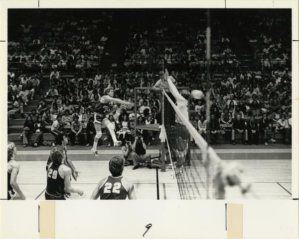 UCLA volleyball player spiking the ball over the net at a game