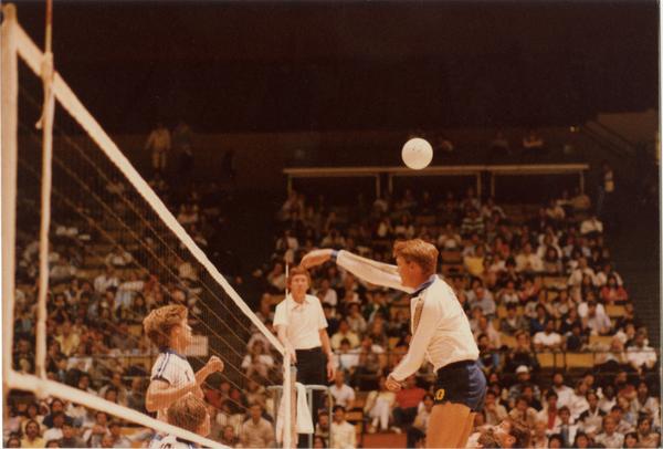 UCLA volleyball player hitting the ball over the net during a game, 1983