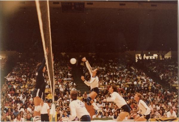 UCLA volleyball player spiking the ball over the net at a game, 1983