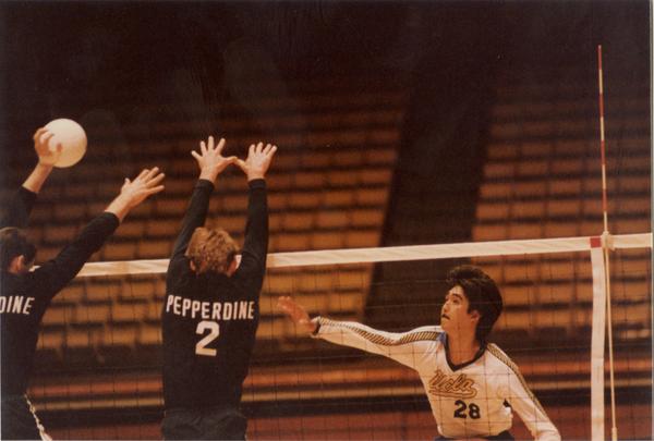 UCLA volleyball player hitting the ball over the net with opposing teammembers attempting to block during a game, 1983