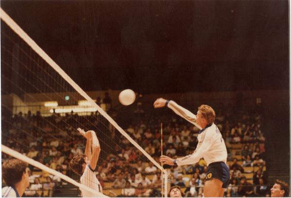 UCLA volleyball player hitting the ball over the net during a game, 1983
