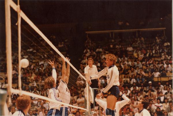 UCLA volleyball player spiking the ball over the net during a game, 1983