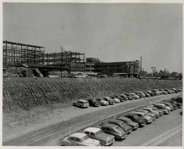 Construction sign for the UCLA medical center with cars parking in the dirt, c. 1951