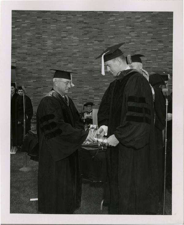 Graduate student receives his diploma from the academic procession during the ceremony, 1956