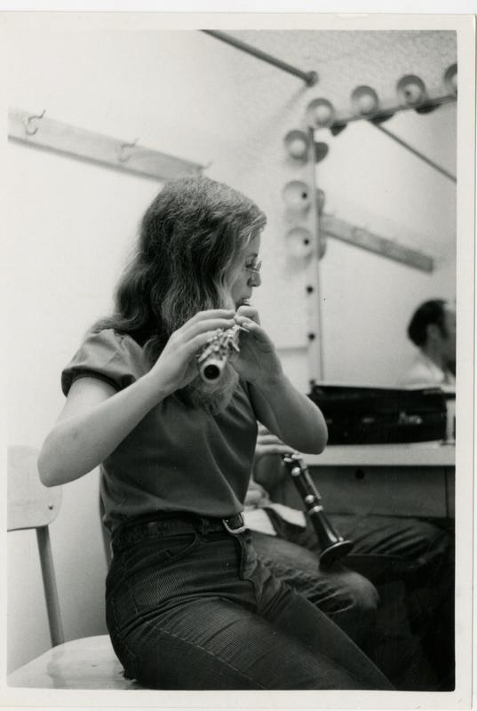Member of the Jazz Ensemble playing the flue with a clarinet resting on her knee during a practice