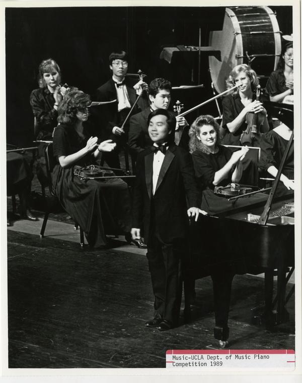 Unidentified student stands up next to his piano with other musicians in the background during the Department of Music Piano Competition, 1989