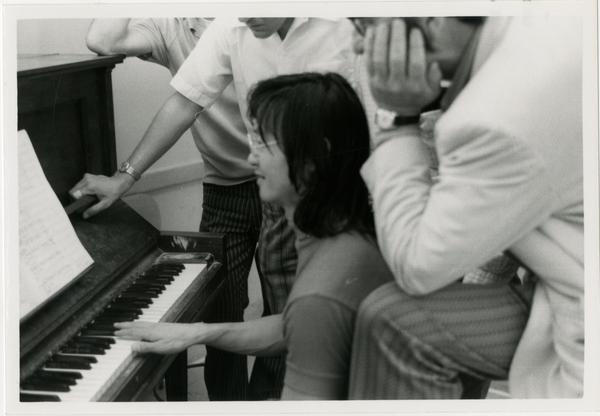 Student sits at the piano while an instructor looks over her shoulder during composition class, 1972
