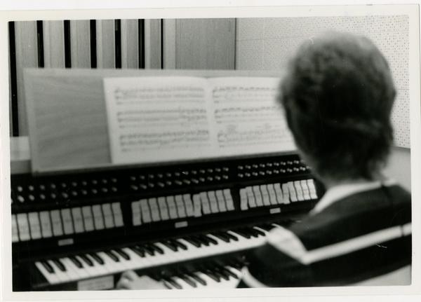 Student looks at the music sheet and plays the piano in the practice room, 1972