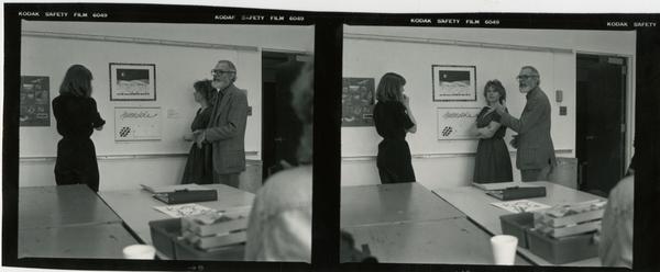 Professor John Neuhard talking with two women, possibly students, as they look at framed art on the wall