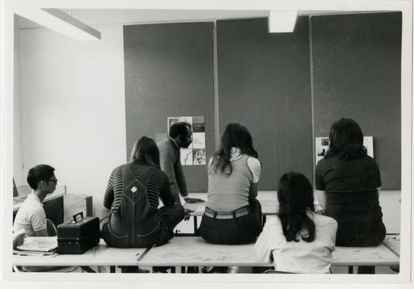 Professor Brown and a group of students examine art posters in a classroom