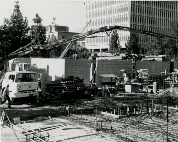 Construction workers and equipment on site of Schoenberg Hall with a view of Young Research Library and Bunche Hall in the background