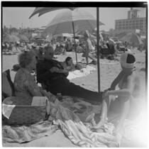 Two women and a man have a picnic under umbrellas at the beach on Labor Day, Los Angeles, September 3, 1945