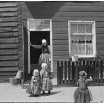 Three little girls and a woman wearing traditional Dutch clothing outside a house, Holland, 1929