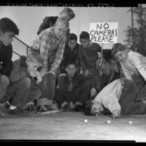 Boys playing in marbles tournament, one with sign reading 