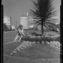 Carolyn Bartett seated on lawn and admiring flowers in the garden at the Municipal Auditorium, Long Beach, 1932