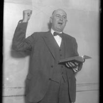 Los Angeles policeman Percy A. Ackley standing with bible in left hand and right fist raised as he preaches in 1930
