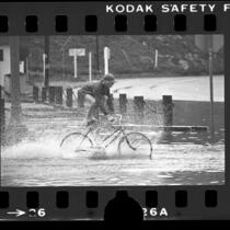 Boy riding bicycle through flooded street in Playa del Rey, Calif., 1976