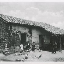 Man and children in front of adobe house.