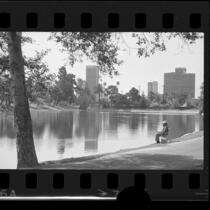 Man fishing in Echo Park lake with buildings of Bunker Hill in background in Los Angeles, Calif., 1975