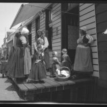 Women and young girls in traditional clothing gathered on a store porch talking, Europe, late 1920s