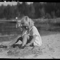 Girl playing with sand on lakeshore, Lake Arrowhead, 1929