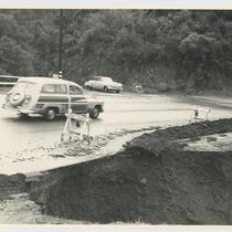 Automobile driving through street damaged by flood, Beverly Glen, Los Angeles, 1952