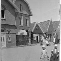Two little girls wearing traditional Dutch clothing outside a row of buildings in Holland, 1929