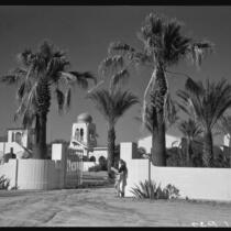 El Kantara, house with onion dome, horseshoe arches, and tiled roof, with woman at gate, Palm Springs, [1930s or 1940s?]