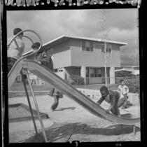 Four boys playing on slide in playground at San Fernando Gardens Housing Project, Calif., 1964