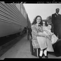 11 year-old actress Margaret O'Brien seated on suitcase holding a doll at Los Angeles Union Station, 1948