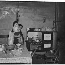 Poverty-stricken woman and child pictured inside a kitchen, Los Angeles, 1930s