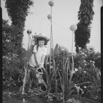 Helena Burnett watering flowers in a garden, 1947-1950