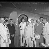 Howard Hughes and group of men standing beside airplane upon Hughes arrival in Los Angeles on August 2, 1938