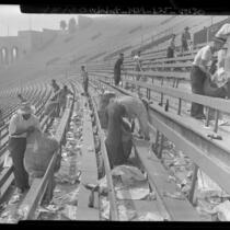 Workmen cleaning up the rubbish and bottles in the stands after a football game at Los Angeles Coliseum