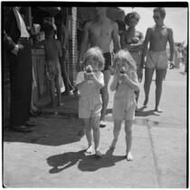 Two young girls in matching overalls eat snow cones on Labor Day, Los Angeles, September 3, 1945