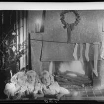 Montage photograph of Mawby triplets in front of fireplace with Christmas tree and stockings, Santa Monica, 1928