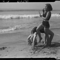 Young women at beach, performing back bend and applying makeup, Venice, 1930
