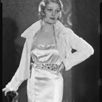Actress (?) modeling a satin evening gown with jeweled sash and a fur jacket, circa 1931-1933