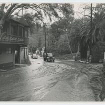 Automobiles drive through the street after flood, Beverly Glen, Los Angeles, 1952