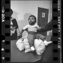 Infant, Dedrionne Stovall, sitting on bags of pennies as part of HUD housing demonstration in Los Angeles, Calif., 1972