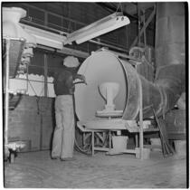 Employee sprays a ceramic toilet bowl with a hose at the Universal-Rundle factory, Redlands, 1940s
