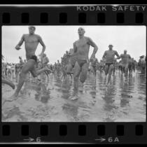Athletes in swimsuits sprinting along beach at start of the Bud Light U.S. Triathlon Series in Long Beach, Calif., 1984